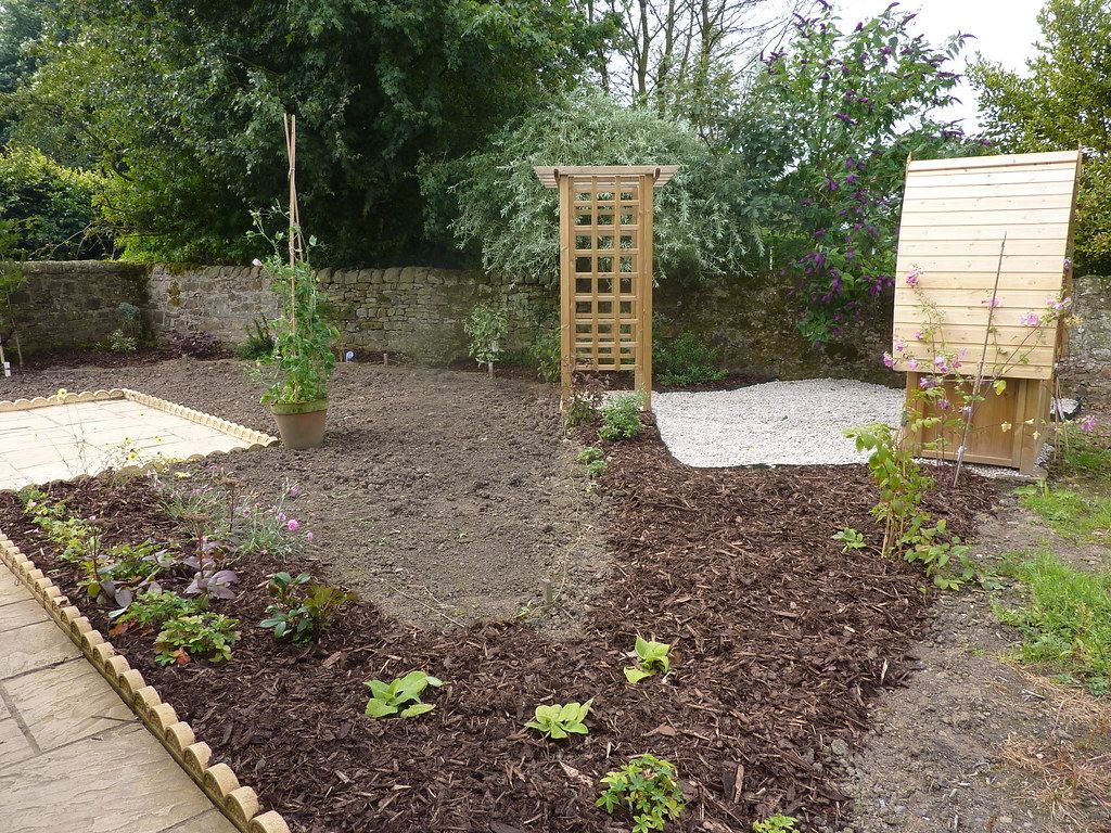 Freshly mulched and planted garden beds along a stone wall